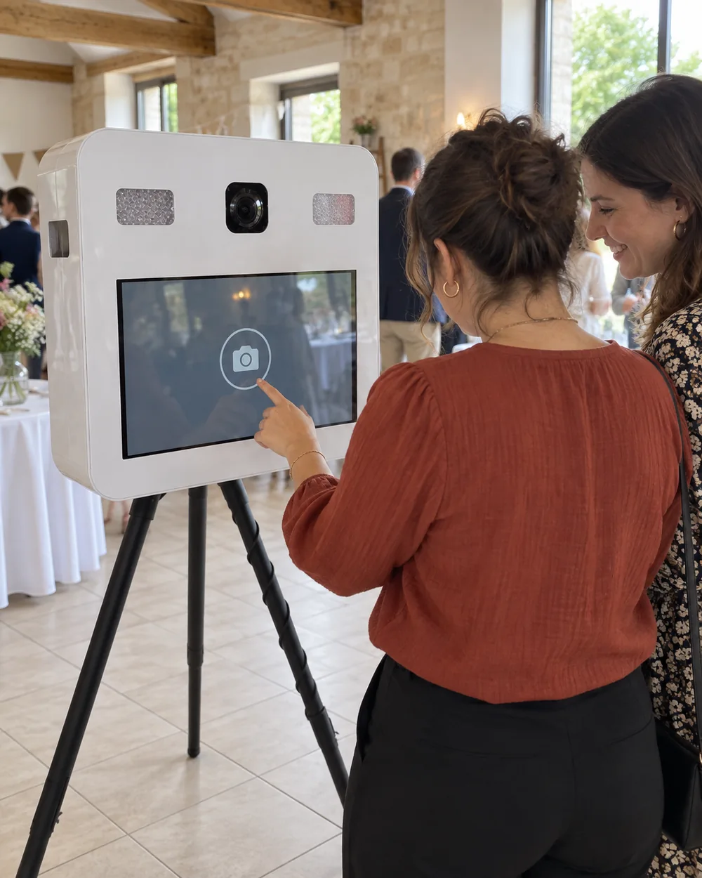 Une invitée touche l’écran du photobooth blanc tandis qu’une autre regarde